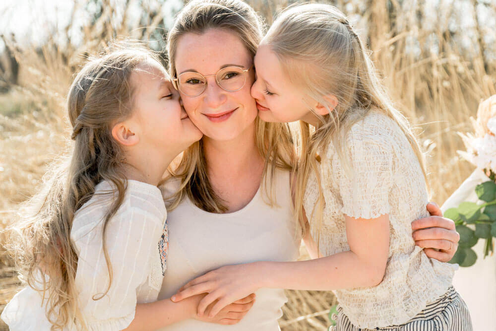 Die Töchter geben ihrer Mama ein Küsschen auf die Wange beim Fotoshooting - Familienfotos & Babybauchfotos in Rostock