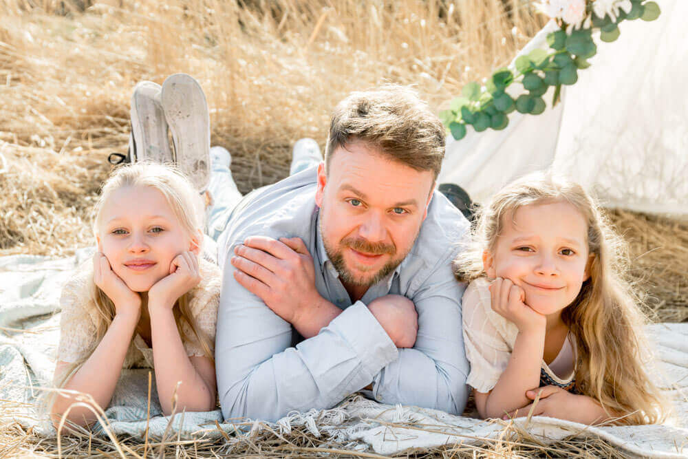 Papa und seine 2 Töchter liegen auf dem Boden im Feld - Familienfotos & Babybauchfotos in Rostock