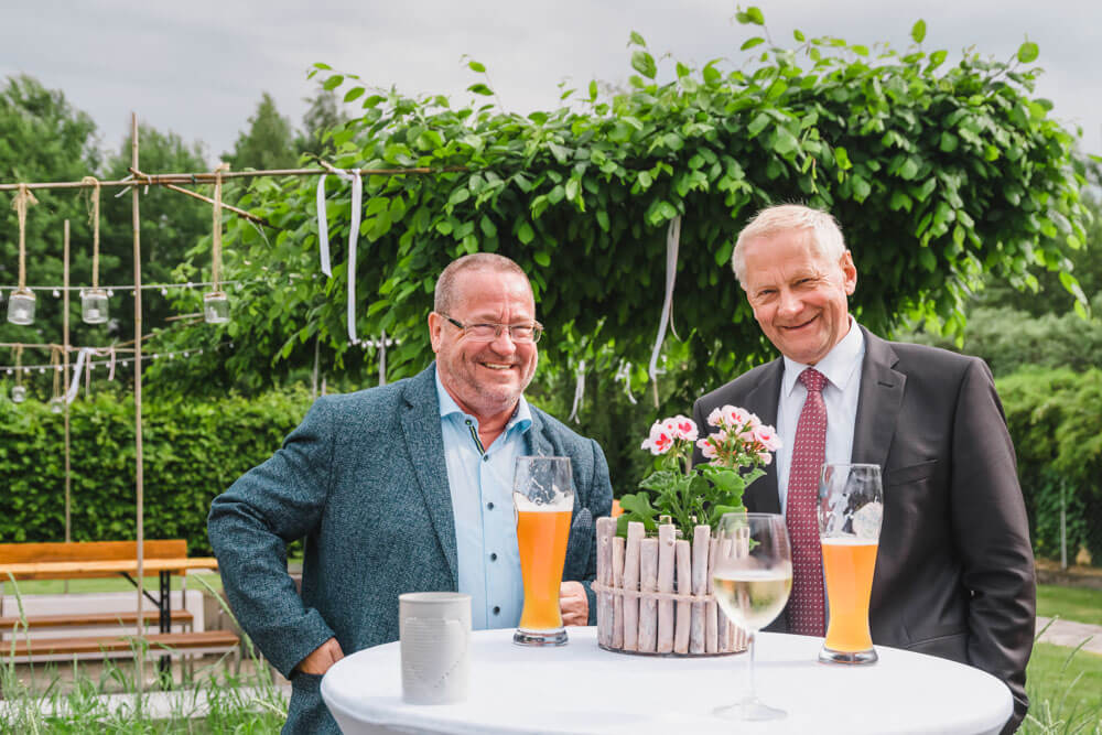 Die Väter von Braut und Bräutigam unterhalten sich während der Gartenhochzeit mit einem Bier in der Hand. Hochzeitsreportage. Hochzeitsfeier in Zingst an der Ostsee