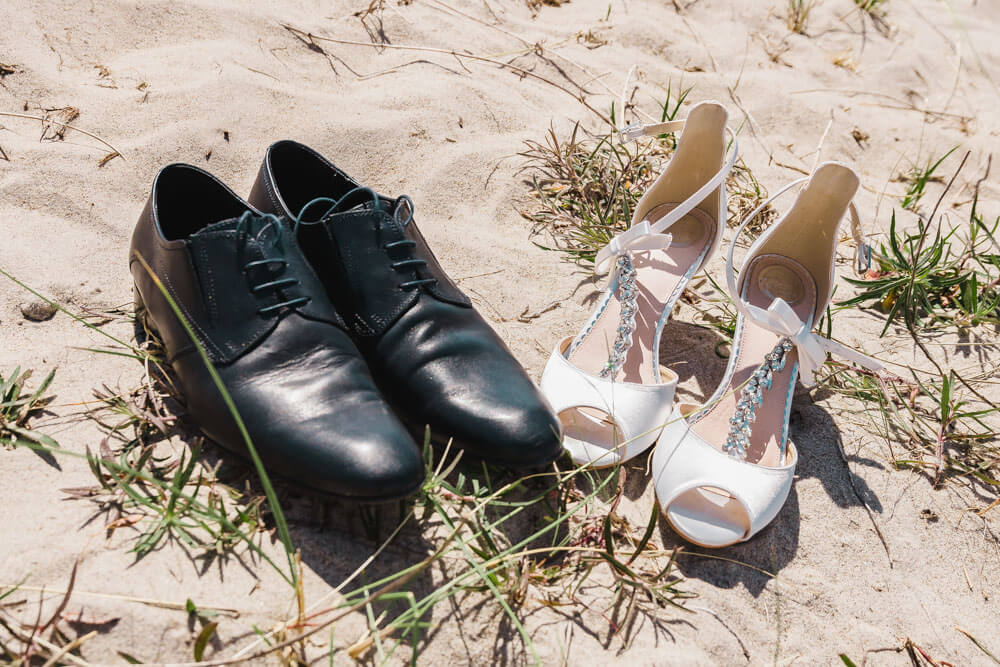 Hochzeit am Strand. Brautschuhe und Schuhe des Bräutigams im Sand. Das Brautpaar läuf barfuß durch den Ostseesand.