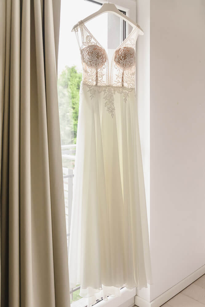 Brautkleid hängt vor dem Fenster, bevor es gleich angezogen wird. Hochzeitsreportage auf dem Darss an der Ostsee.