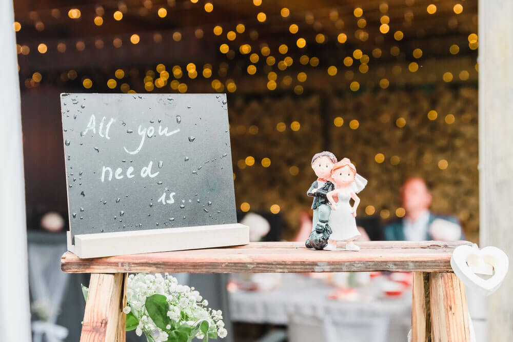 "All you need is..."-Schild als Dekoration bei einer Gartenhochzeit. Hochzeitsfotografie in Zingst an der Ostsee bei Regen.