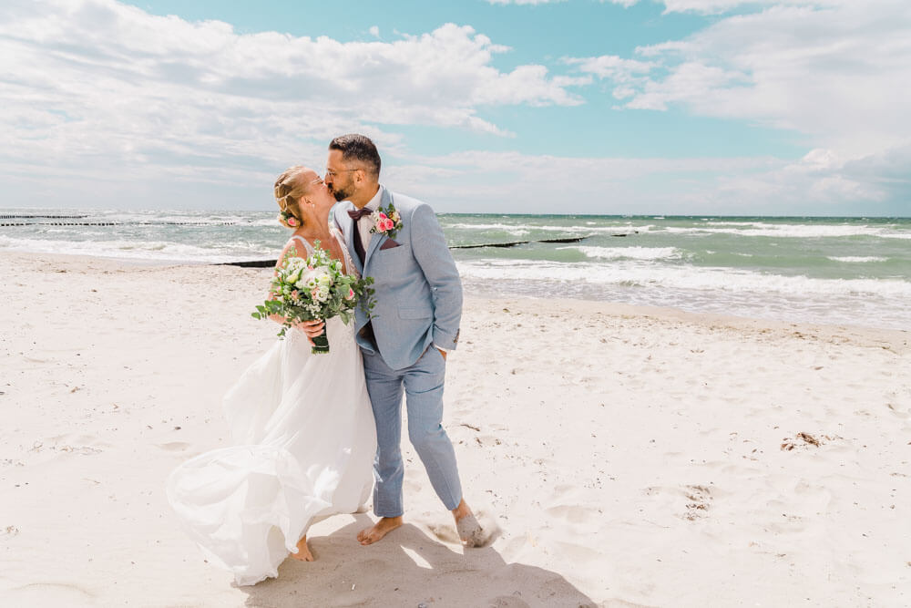 Das Hochzeitspaar küsst sich am Strand. Brautpaarfotos am Ostseestrand auf dem Darss in Mecklenburg-Vorpommern. Hochzeitsfotograf an der Ostsee (Markgrafenheide, Graal-Müritz, Dierhagen, Ahrenshoop, Wustrow, Prerow, Zingst).
