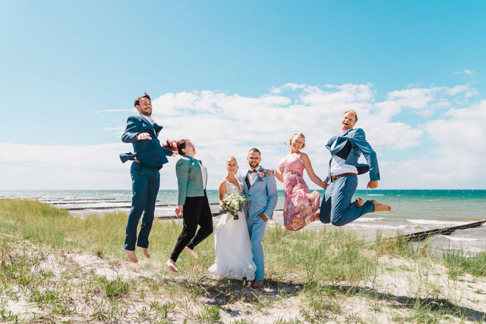 Hüpfende Hochzeitsgäste. Gruppenfoto zur Hochzeit am Strand von Ahrenshoop in den Dünen. Hochzeitsfotograf an der Ostsee (Markgrafenheide, Graal-Müritz, Dierhagen, Ahrenshoop, Wustrow, Prerow, Zingst).