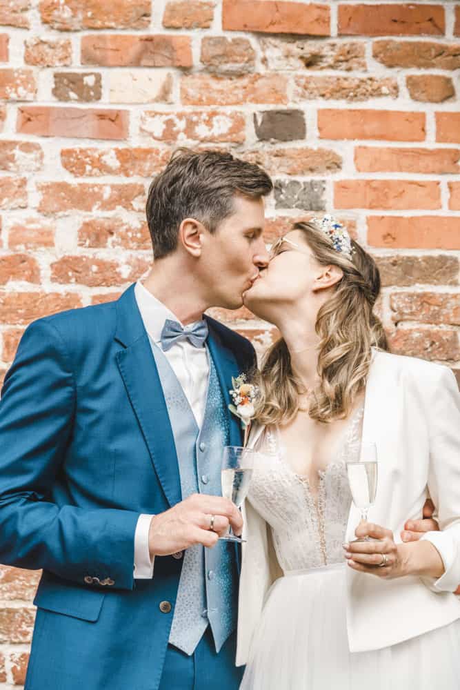Braut und Bräutigam küsst sich beim Sektempfang.