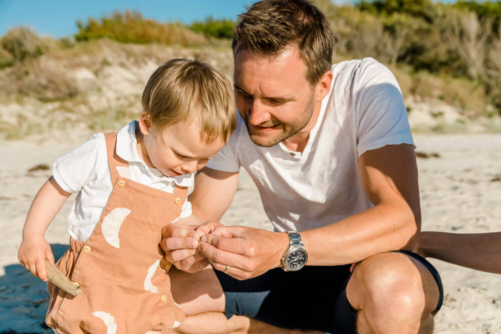 Papa zeigt seinem Sohn eine Muschel am Strand von Ahrenshoop. Als Familienfotograf habe ich diesen süßen Moment festgehalten.