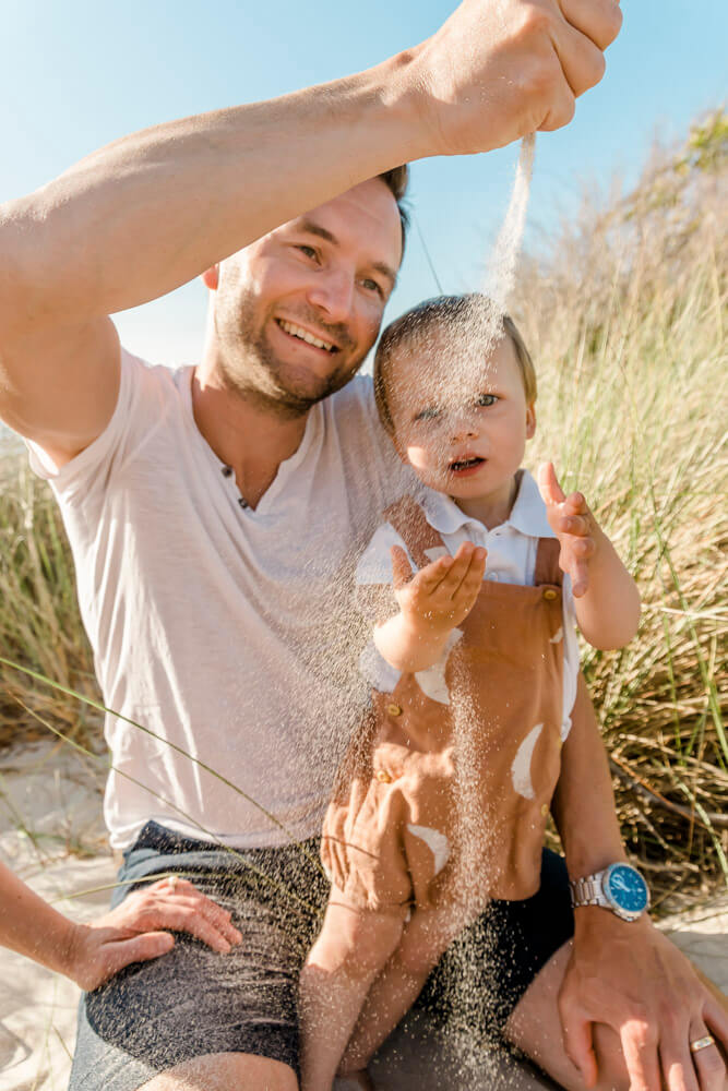 Papa lässt Sand aus seiner Hand rieseln und der Sohn schaut dabei gespannt zu. Eine ungestellte Situation beim Fotoshooting von Fotografin aus Dierhagen.
