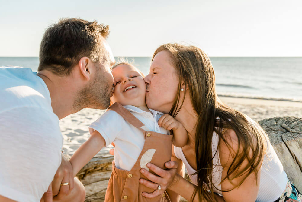 Mama und Papa küssen ihren Sohn auf die Wange am Strand von Dierhagen beim Familienfotoshooting.