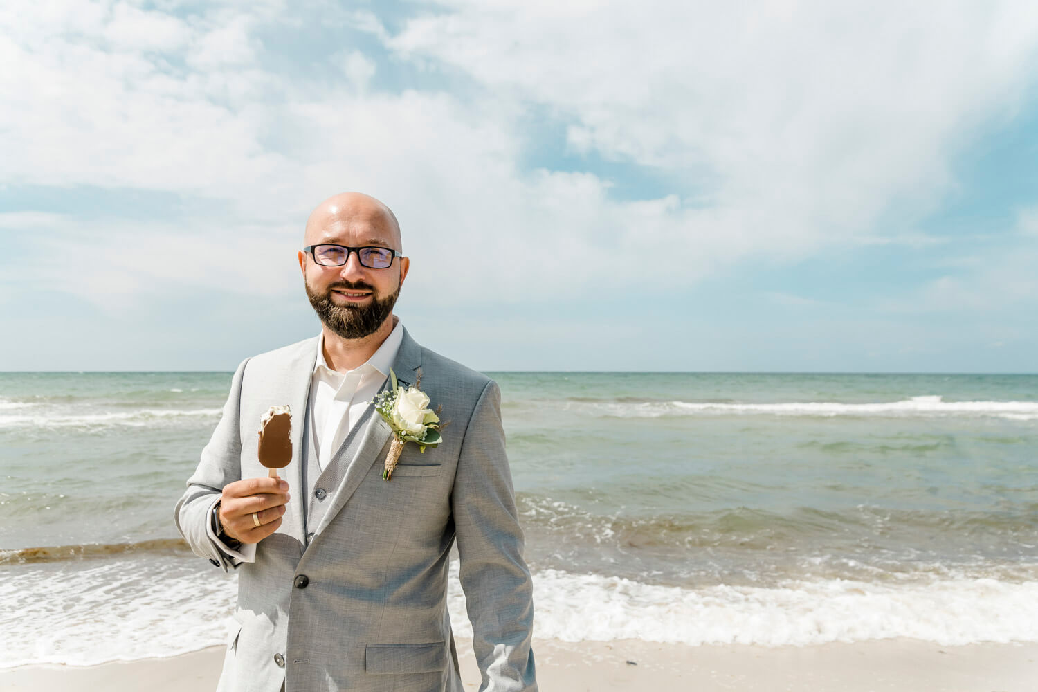 Der Bräutigam isst ein Eis am Hochzeitstag am Strand. Authentische Hochzeitsfotografie.