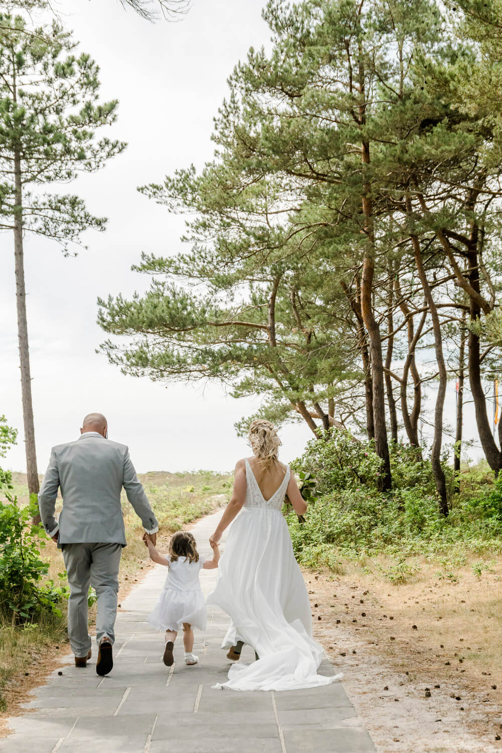 Hochzeitsfoto als Familie. Mama, Papa und Tochter rennen den Weg zum Strand von der Hochzeitslocation "Strandhotel Fischland".