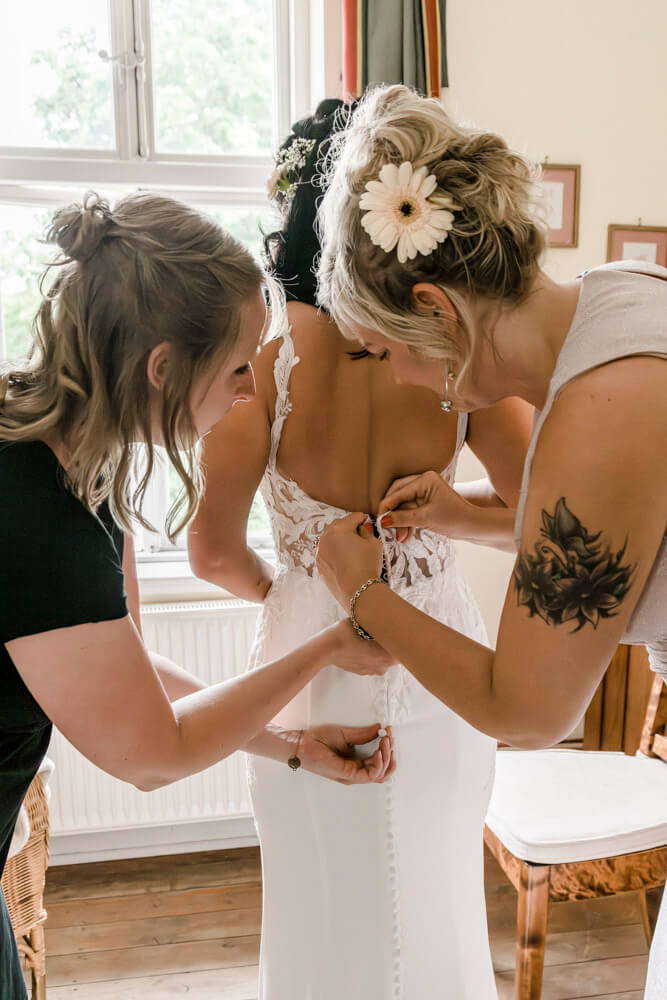 Die Trauzeugin hilft der Braut ins Brautkleid beim Getting Ready für die Hochzeit in Mecklenburg-Vorpommern.