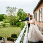 Das Brautpaar steht zur Hochzeit auf der Terrasse vom Gut Pütnitz in Ribnitz-Damgarten und winkt ihren Hochzeitsgästen im Garten zu. Hochzeitsfotograf aus der Region.