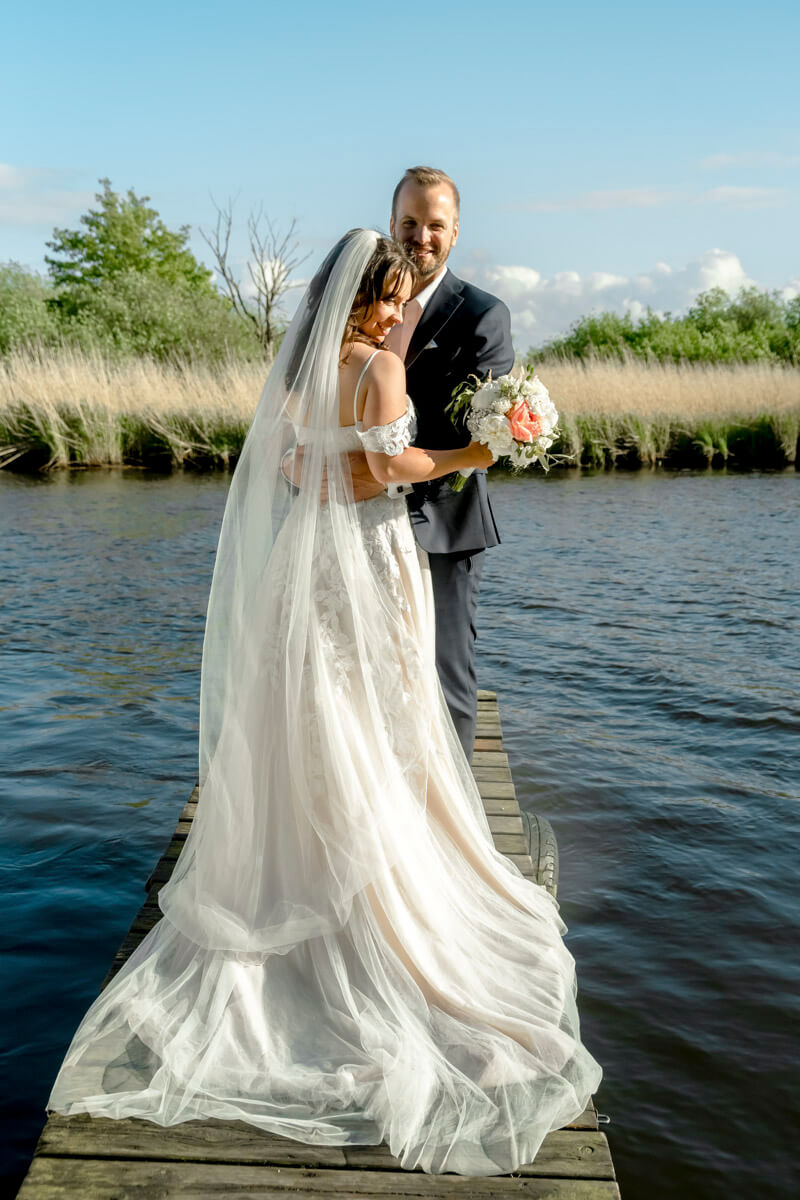 Das Brautpaar steht zum Fotoshooting auf einem kleinen Steg am Wasser.