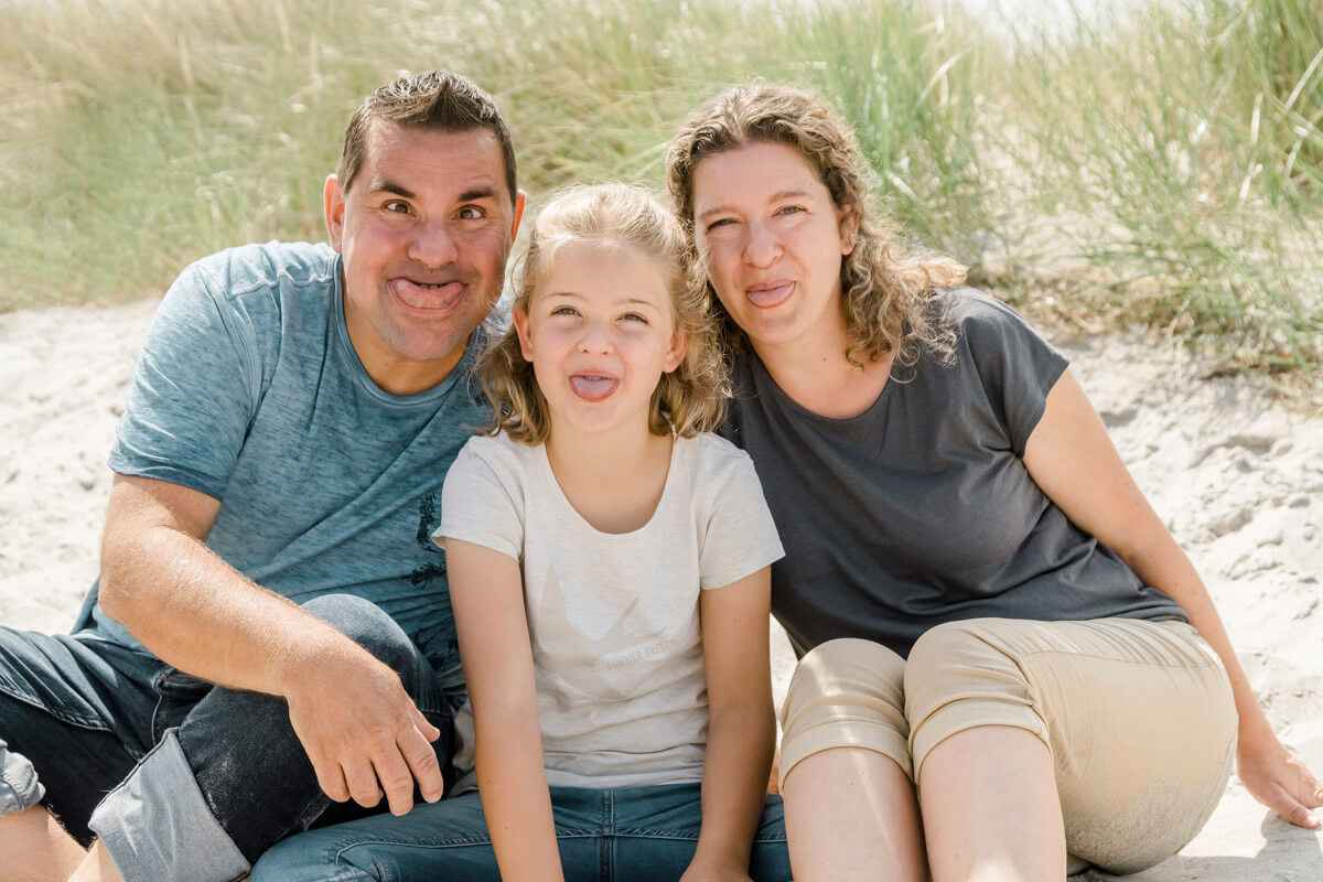 Lustiges Familienfoto am Strand von Ahrenshoop. Mama, Papa und Tochter strecken die Zunge heraus.