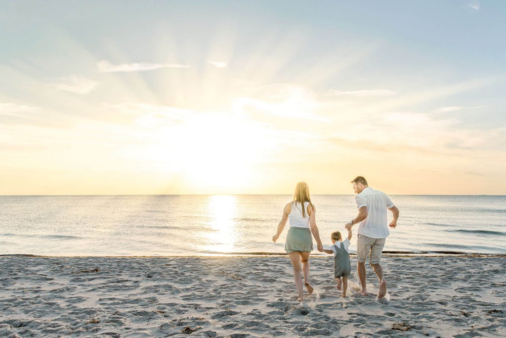 Familie beim Spaziergang am Strand während des Sonnenuntergangs, Kinder und Eltern genießen die Zeit am Meer.