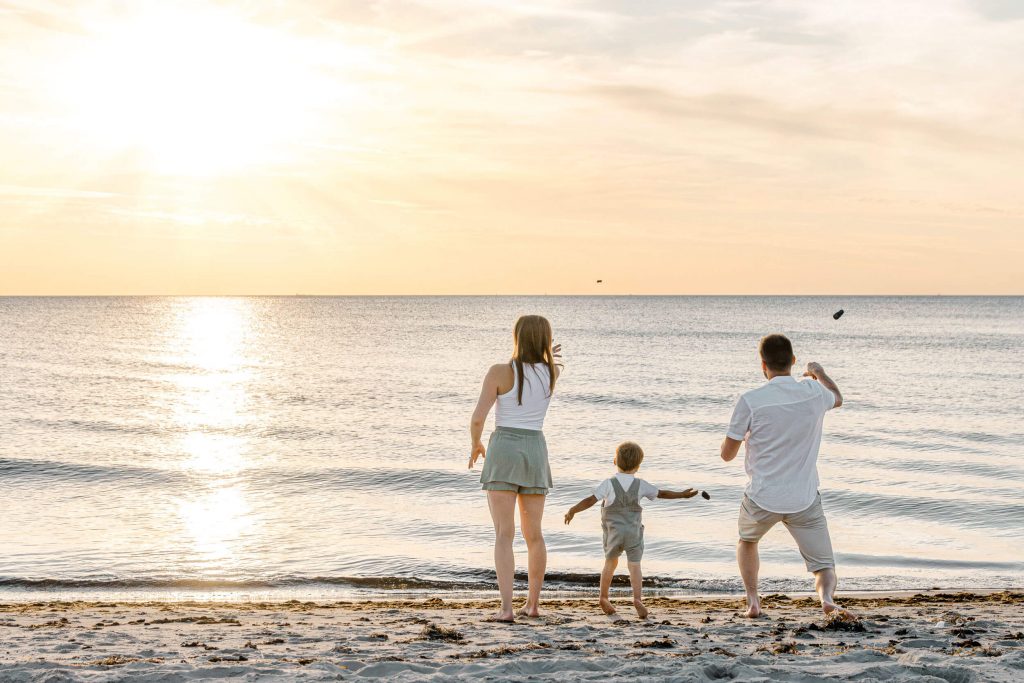 Familie am Strand bei Sonnenuntergang, Eltern und Kind spielen am Wasser, entspannte Atmosphäre, Familienfotografie, Strandfotos.