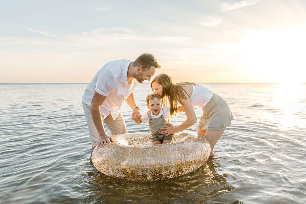 Familie mit Kind in einem Schwimmreifen im Wasser bei Sonnenuntergang, ideal für Familienfotos und Strandaufnahmen.