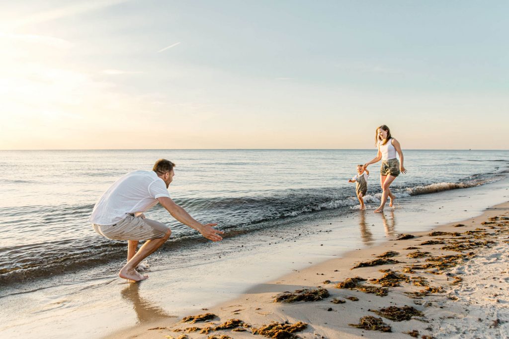 Familie am Strand mit einem Kind, das im Wasser spielt, während die Eltern sich freuen und interagieren. Ein schöner Strandtag.