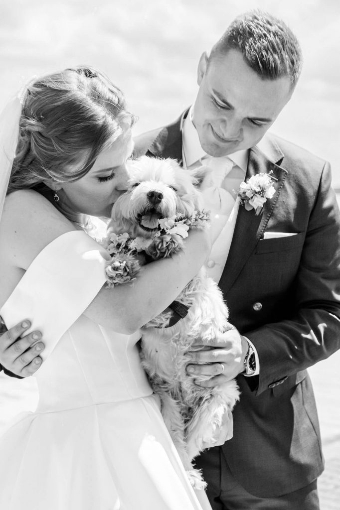 Brautpaar umarmt Hund in Hochzeitskleidung draußen