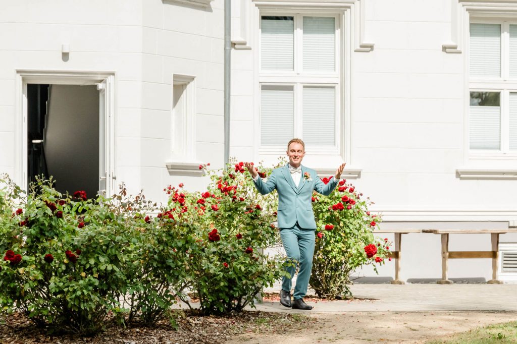 Person im Anzug vor weißem Gebäude und Rosen