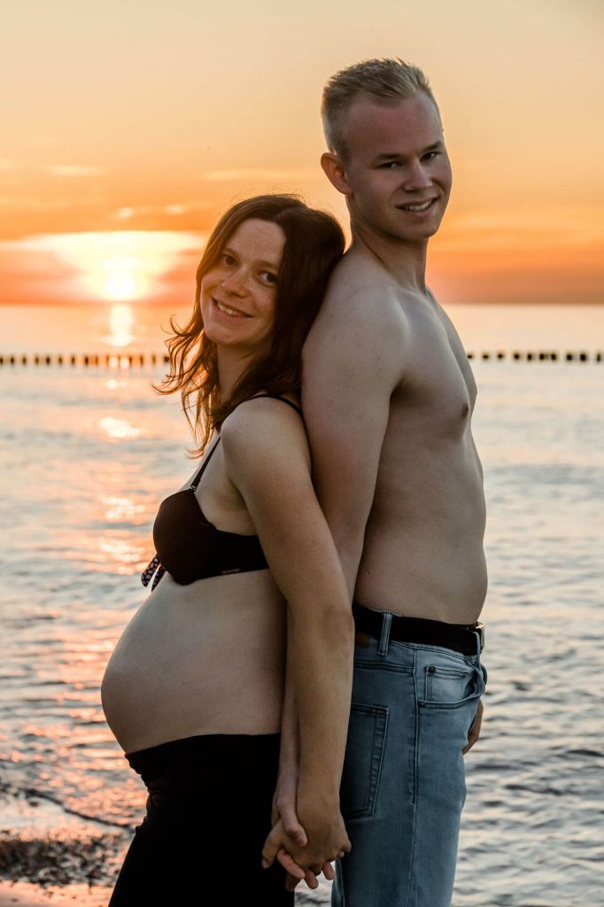 Junges Paar bei Sonnenuntergang am Strand zum Babybauch Fotoshooting in Warnemünde