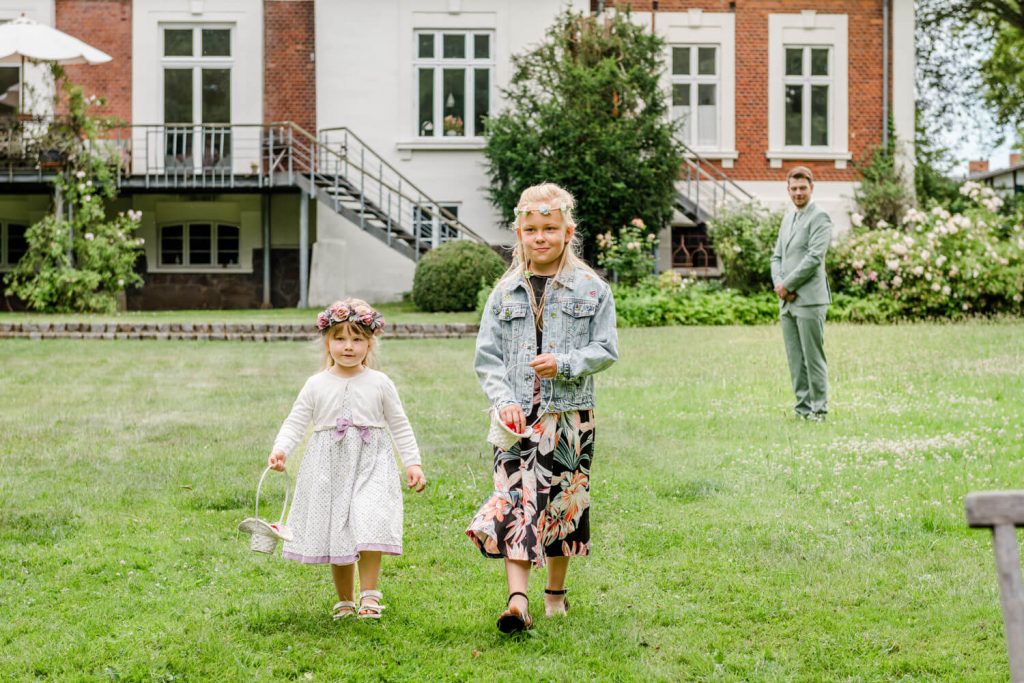Gut Groß Siemen. Zwei Kinder laufen über Rasen in Sommerkleidung. Blumenmädchen zur freien Trauung im Garten.