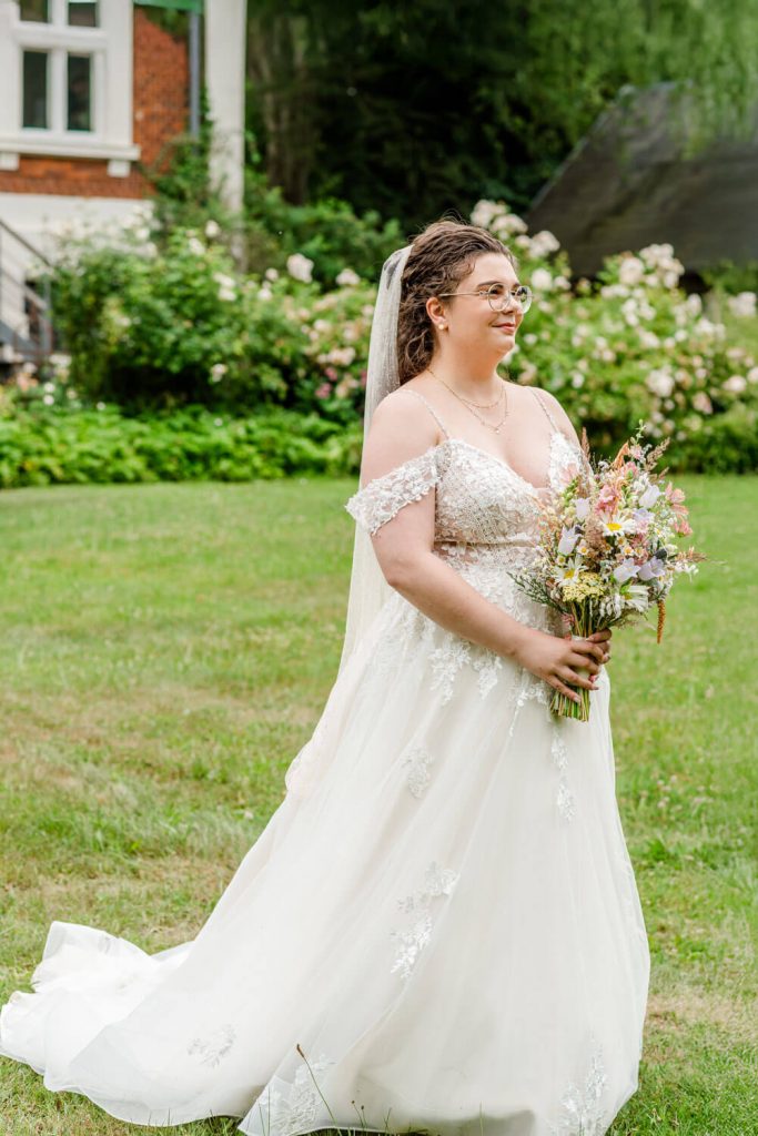 Braut im Garten mit Blumenstrauß am Hochzeitstag. Gut Groß Siemen.