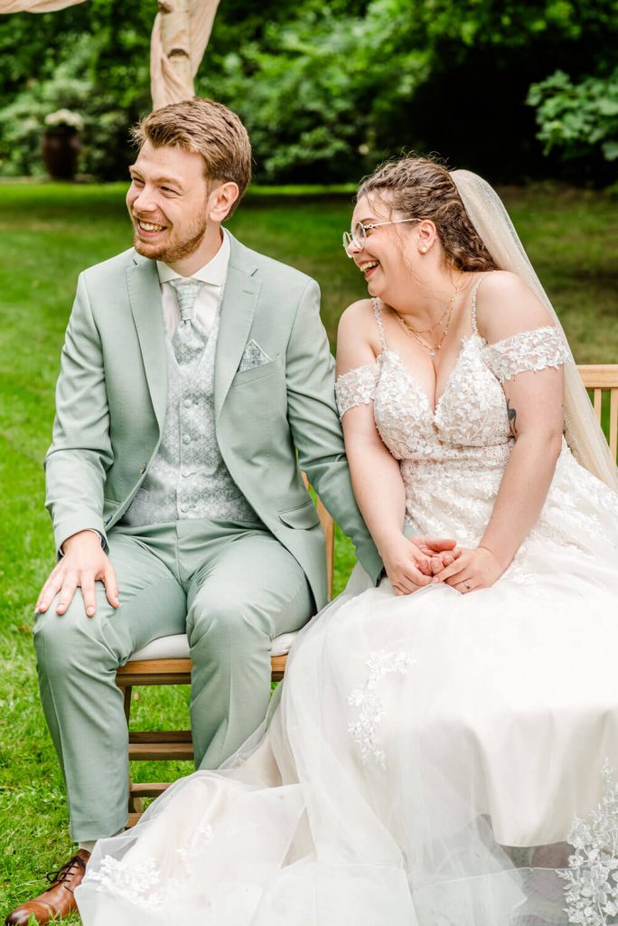 Lachendes Hochzeitspaar im Freien auf einer Bank