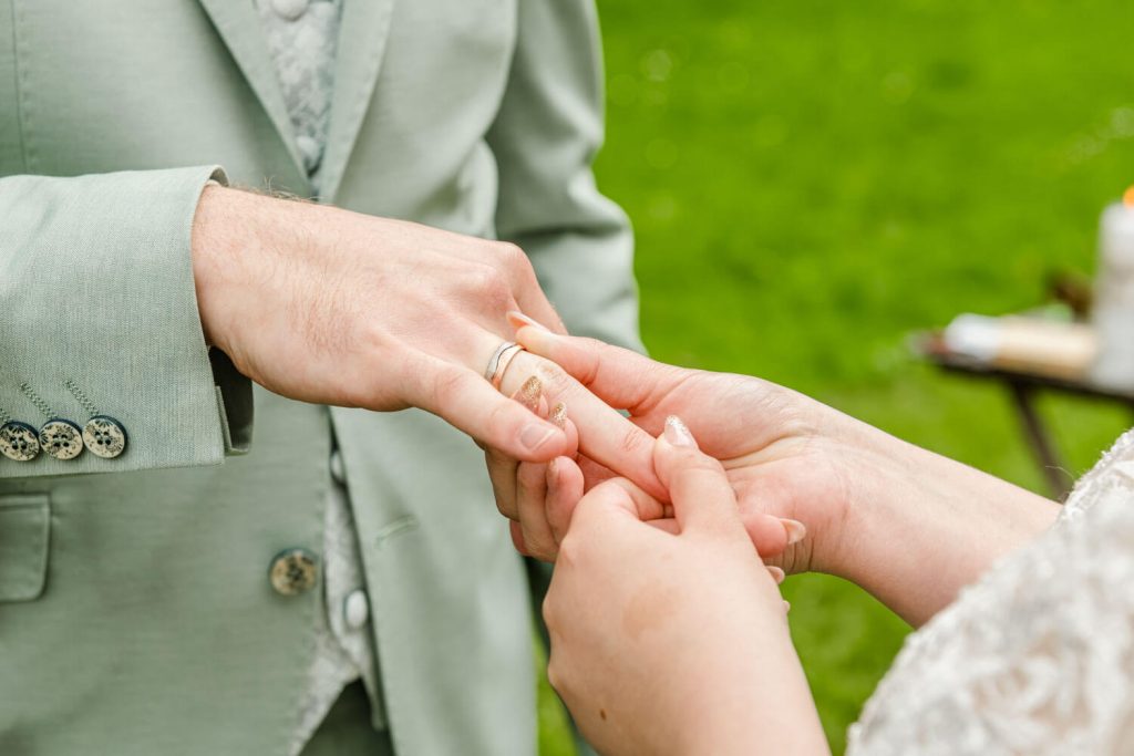 Bräutigam steckt Braut Ehering an während Hochzeit