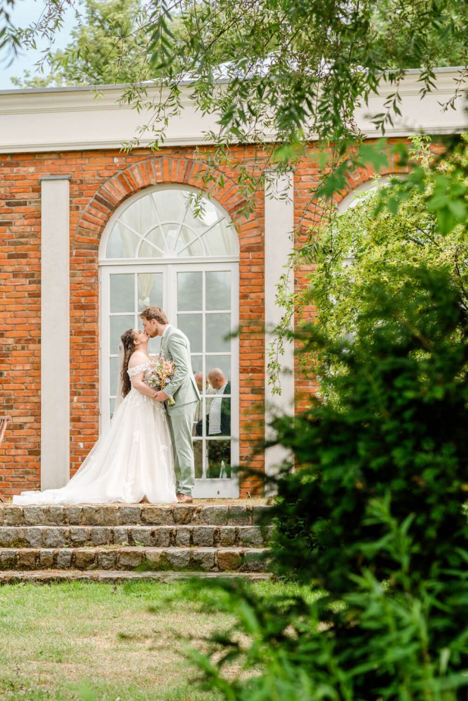 Gut Groß Siemen. Brautpaar posiert draußen vor Backsteingebäude.