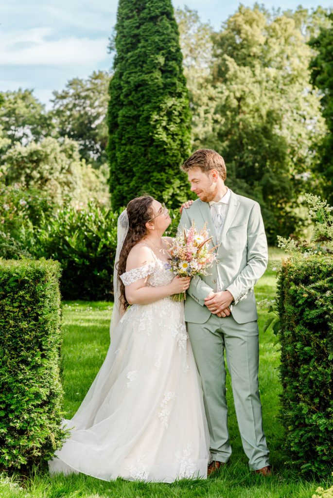 Gut Groß Siemen. Brautpaar lächelt im Garten bei sonnigem Wetter
