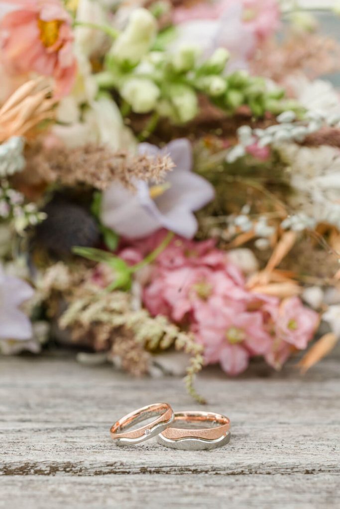 Zwei Eheringe vor buntem Blumenstrauß Hintergrund