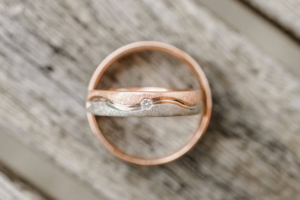 Zweifarbiger Ehering mit Diamant auf Holzoberfläche