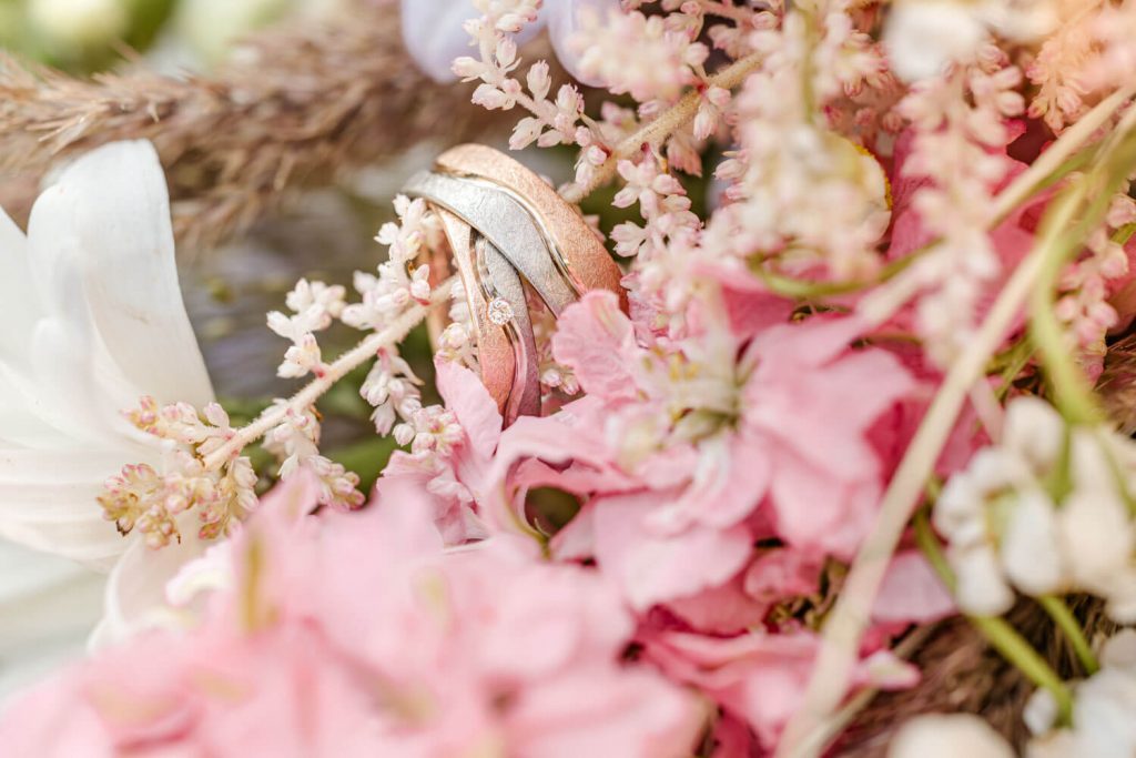 Verlobungsringe inmitten zarter rosa Blütenarrangementen flankiert