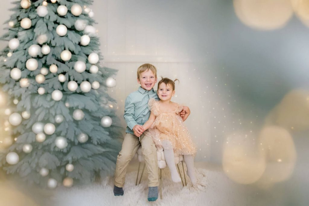 Zwei Kinder posieren fröhlich neben Weihnachtsbaum