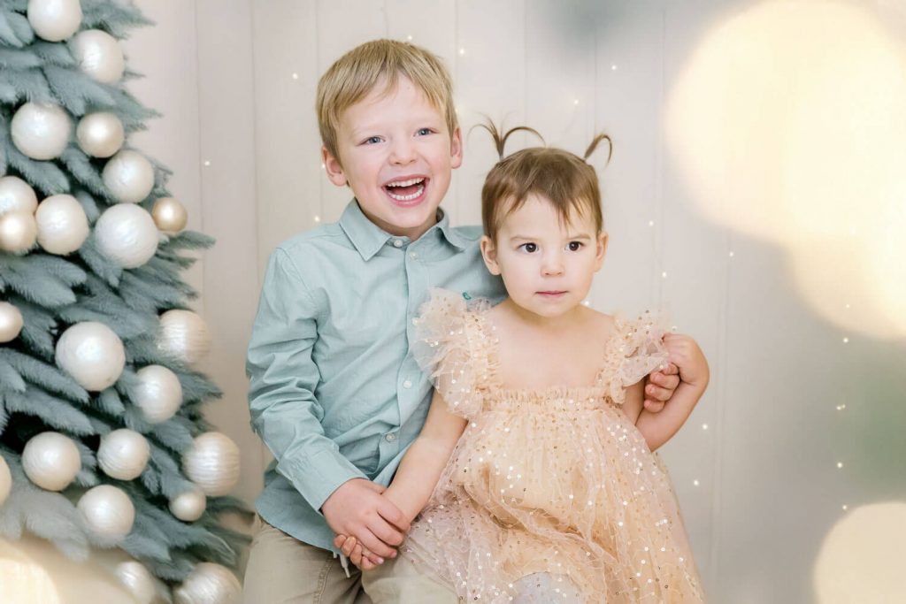 Lächelnde Kinder posieren neben geschmücktem Weihnachtsbaum