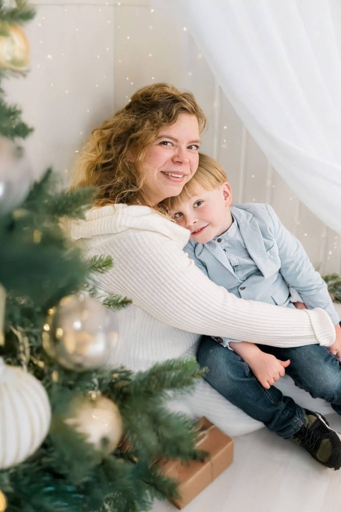 Mutter umarmt Kind neben dem Weihnachtsbaum