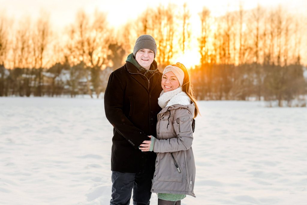Paar im Schnee bei Sonnenuntergang lächelnd fotografiert