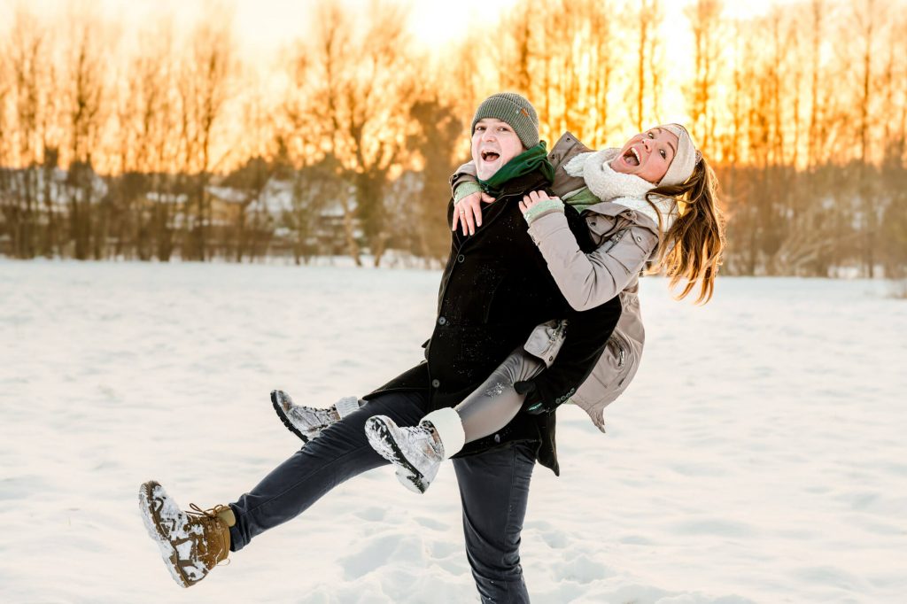 Fröhliches Paar im Schnee bei Sonnenuntergang