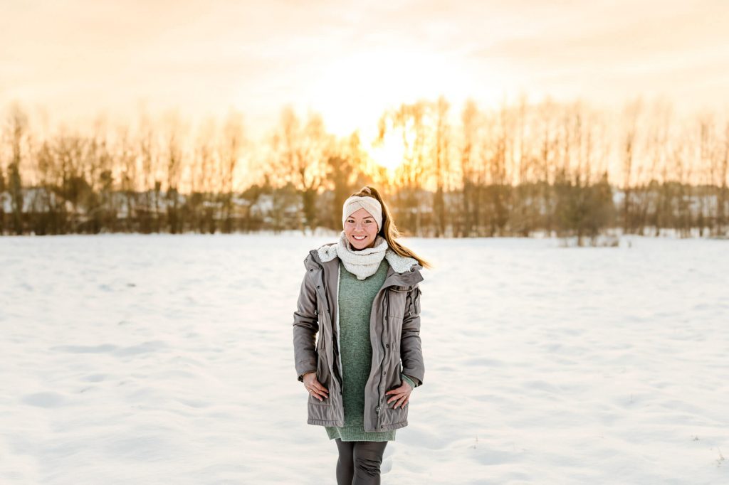 Frau im Wintermantel im verschneiten Sonnenuntergangsfeld
