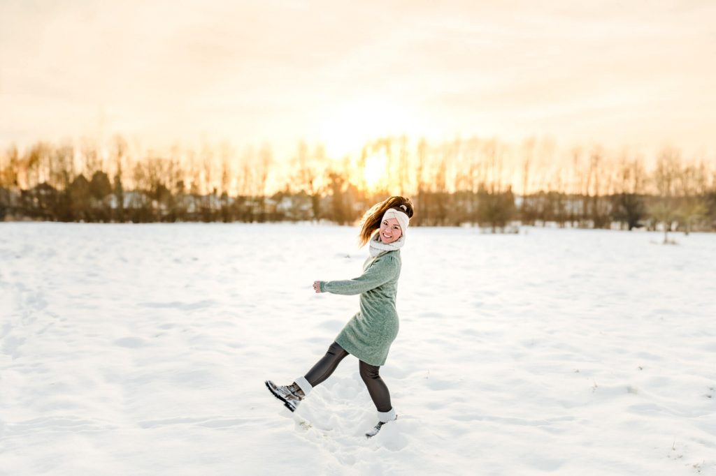 Frau spaziert im Schnee bei Sonnenuntergang glücklich