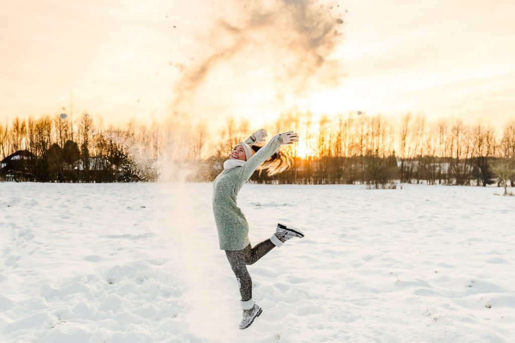Frau tanzt fröhlich im Schnee bei Sonnenuntergang
