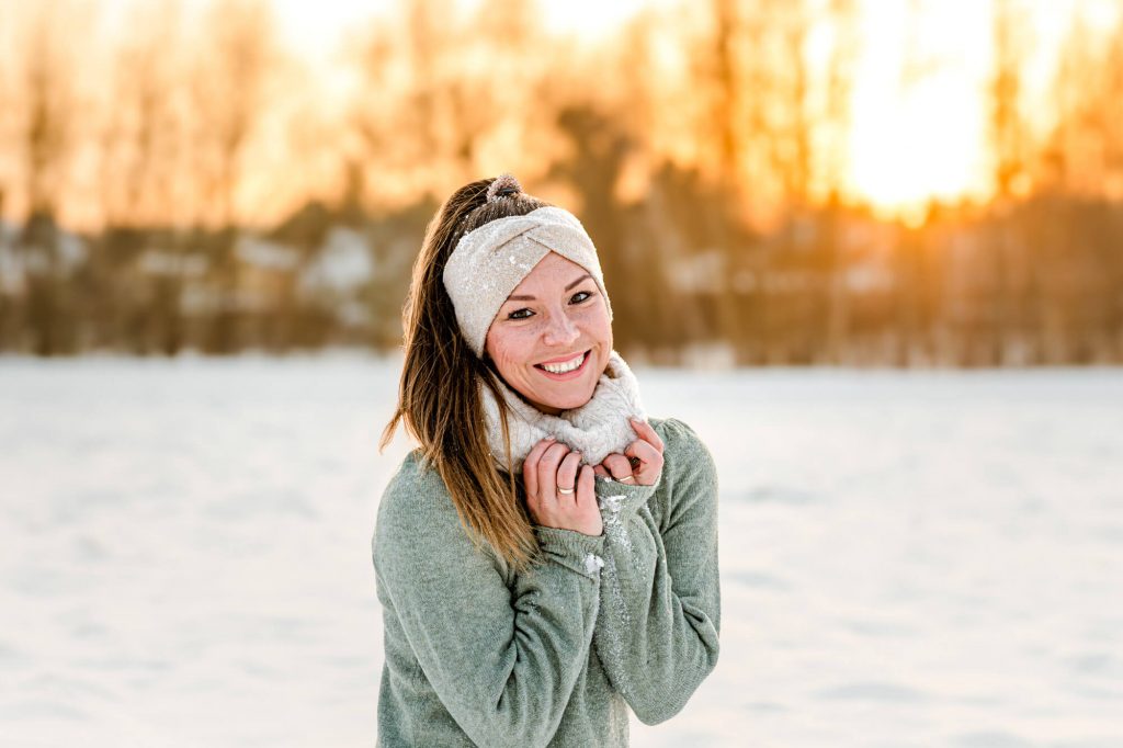 Frau im Schnee lächelt bei Sonnenuntergang draußen