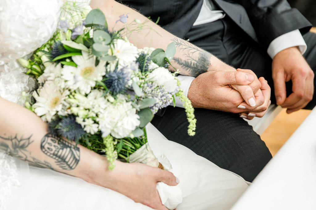 Braut und Bräutigam halten Hände mit Blumenstrauß