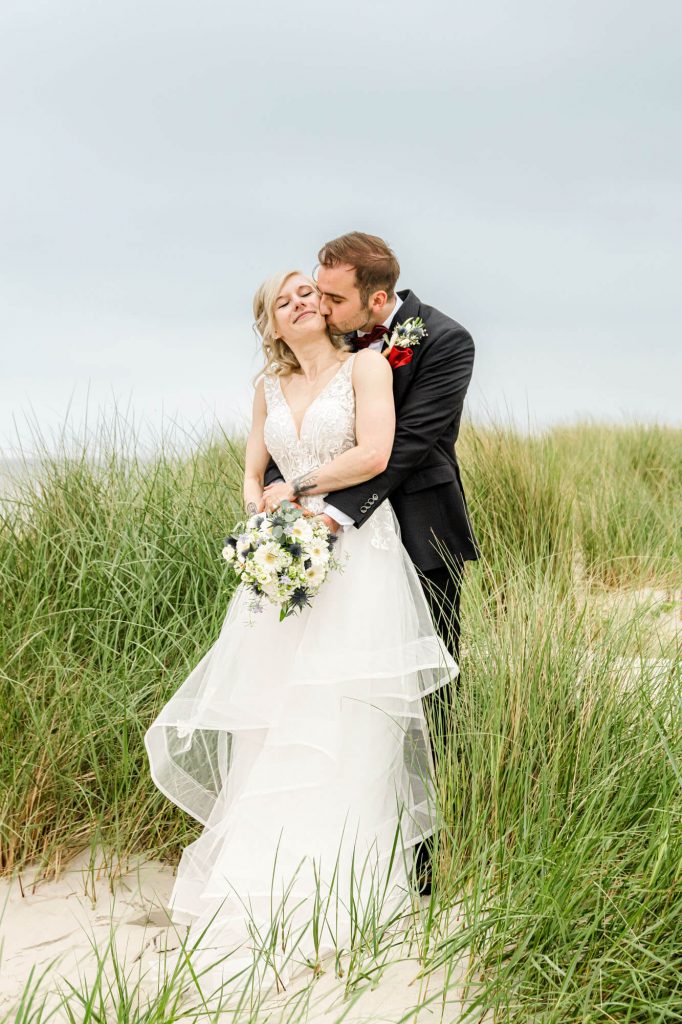 Brautpaar umarmt sich am Strand in Hochzeitskleidung