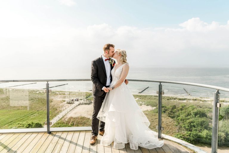 Brautpaar küsst sich auf Balkon mit Meerblick