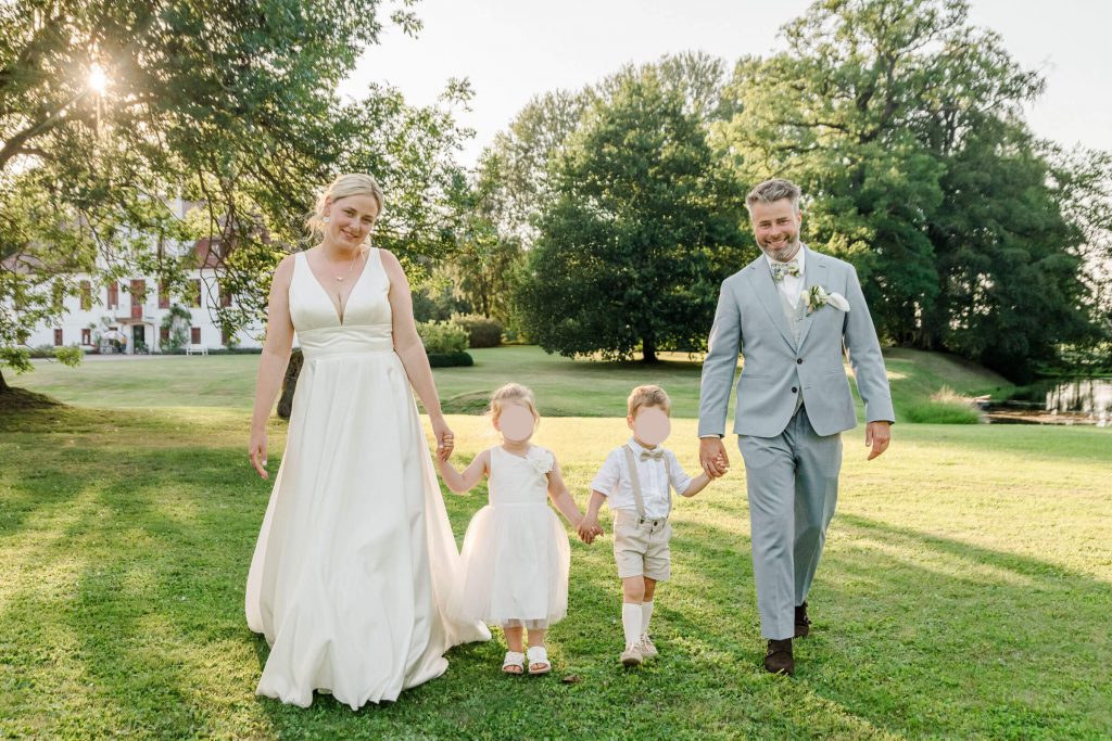 Brautpaar spaziert mit Kindern im sonnigen Park