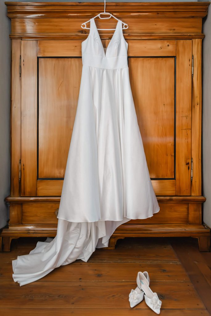 Weißes Hochzeitskleid hängt an Holzschrank