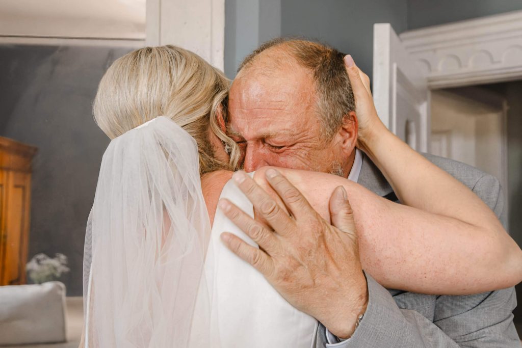 Vater umarmt Tochter mit Hochzeitskleid gerührt