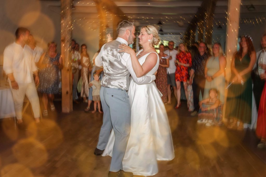 Tanzendes Brautpaar bei Hochzeit mit Gästen im Hintergrund